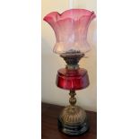 A 19thC brass and cranberry glass oil lamp with etched glass shade. 52cm h to top of shade.