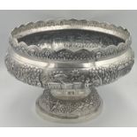 An Indian embossed white metal pedestal bowl decorated with people, elephants, tree and buildings.