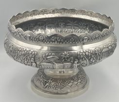 An Indian embossed white metal pedestal bowl decorated with people, elephants, tree and buildings.