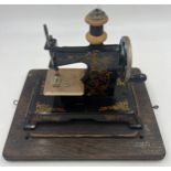 A child’s metal sewing machine in an oak Edison case. 25cm w x 22cm h.