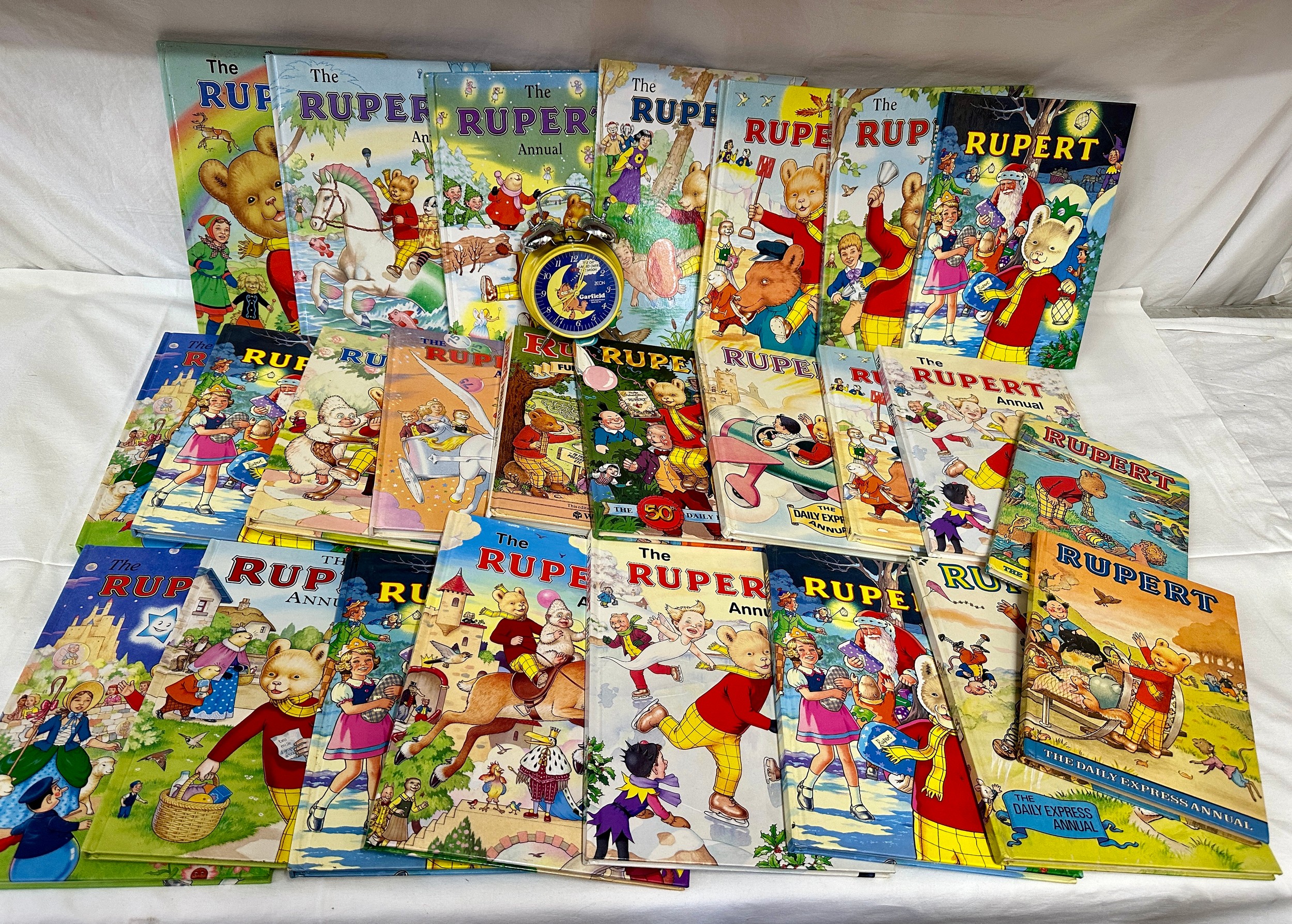 A quantity of Rupert the Bear Annuals and a Garfield 1978 alarm clock. Annuals to include 1975,