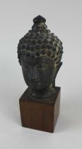 A cast bronze head of a Buddha 19cm high, mounted on wooden plinth