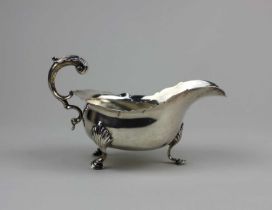 An Edward VII silver sauce boat with flying scroll handle on three shell cast hoofed feet, maker