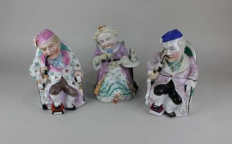 Three novelty character pots of two seated pipe smokers and a woman drinking tea the lids taken from