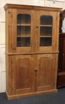 A pine cupboard top section with two glazed doors enclosing shelves above panelled cupboard doors,