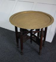 An Eastern brass tray top occasional table on folding wooden stand 59.5cm diameter