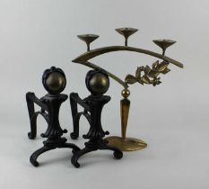 A pair of Arts and Crafts fire dogs and a brass three light candlestick with floral decoration