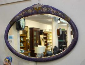 An oval wall mirror the painted purple frame with flower and urn surmount, bevelled mirror plate