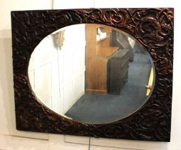 A carved oak rectangular wall mirror with oval glass and surround of carved scrolls and creatures,