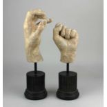 Two realistic modelled composition models of human hands each raised on a fluted ebonised column,