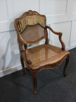 A French style elbow chair with cane seat and fabric panelled back, on carved cabriole legs