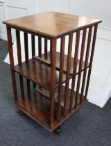 An early 20th century oak revolving bookstand two open tiers with slatted sides on swivel base,