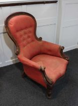 A Victorian button back upholstered chair with scroll carved back frame and arms, on turned legs (