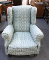 A Howard style wingback armchair with blue and gold floral upholstery on turned front legs and