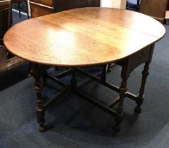 An oak gateleg table, oval shaped top with two drop flaps above a small drawer, on turned supports