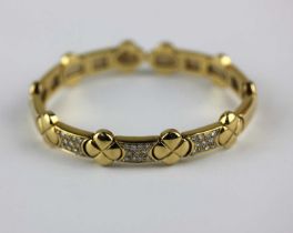 A gold and diamond sprung bangle with quatrefoil shaped links alternating with diamond set panels to