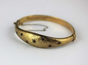 A 9ct gold and ruby oval hinged bangle star set with seven circular cut rubies on a textured ground,