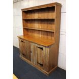 A pine dresser, two tier plate rack with wide boarded back, the base with two panelled cupboard