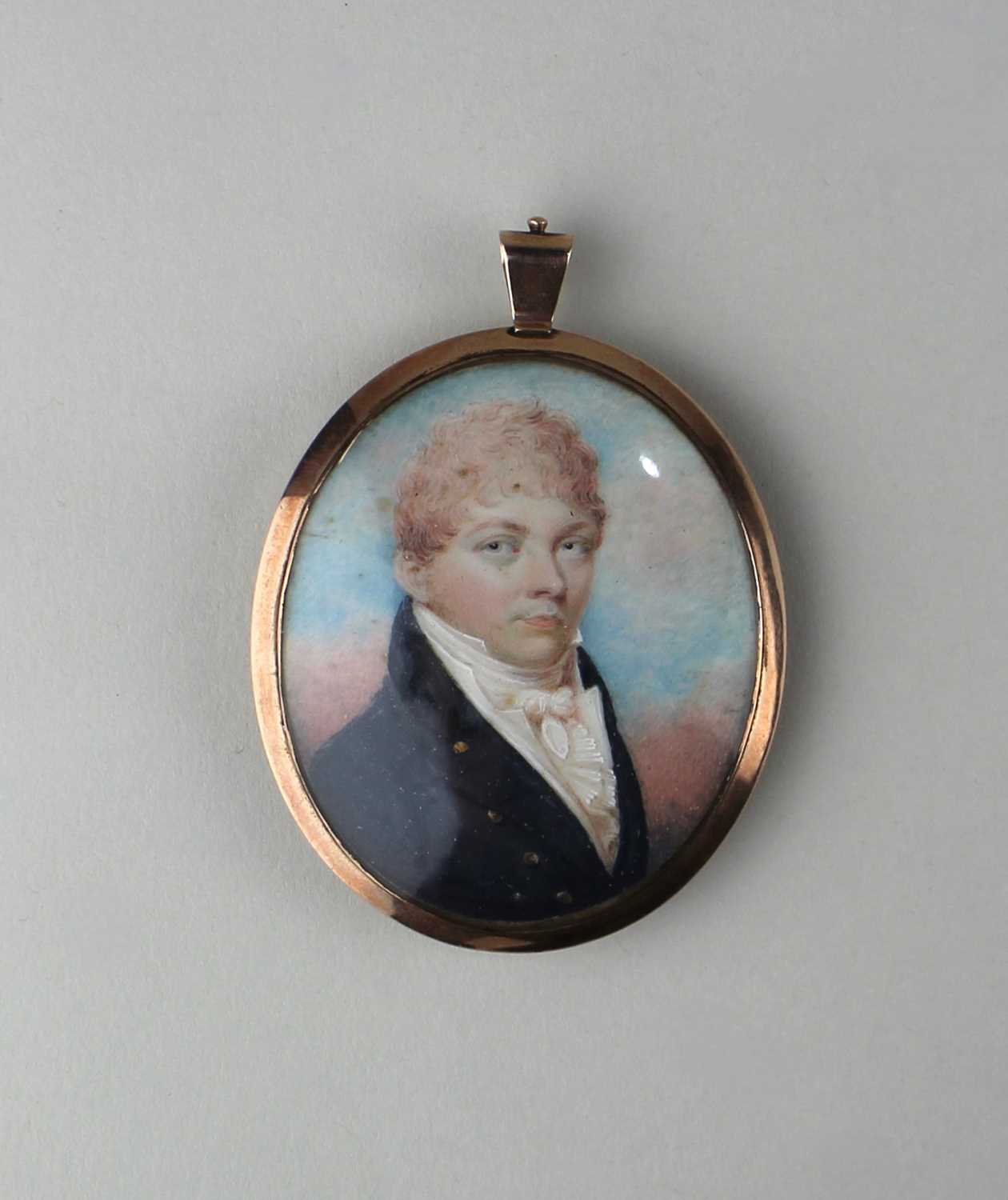 A gold mounted oval portrait miniature of a gentleman with curly pale brown hair wearing a black