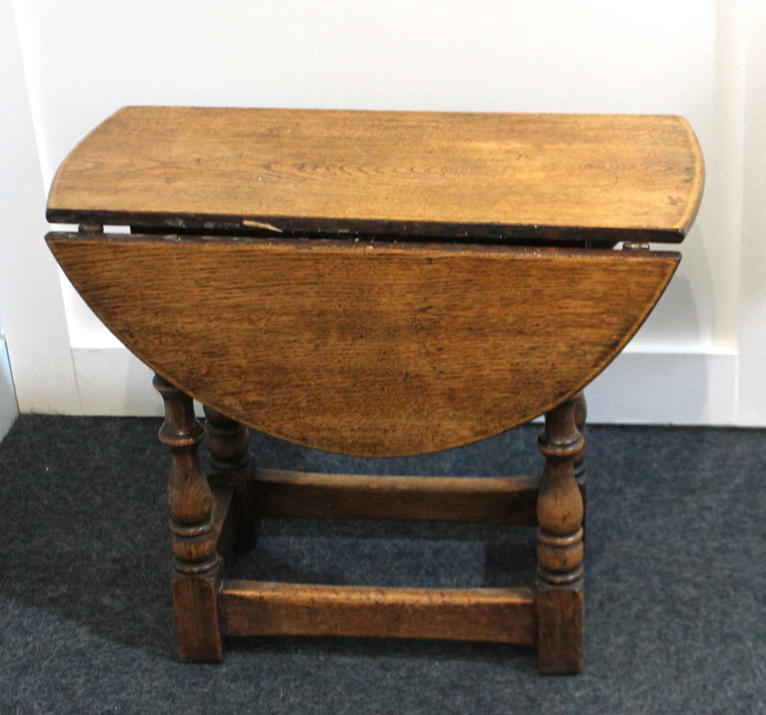 A small oak drop flap occasional table the oval top on turned supports with uniting stretcher 56cm