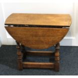 A small oak drop flap occasional table the oval top on turned supports with uniting stretcher 56cm