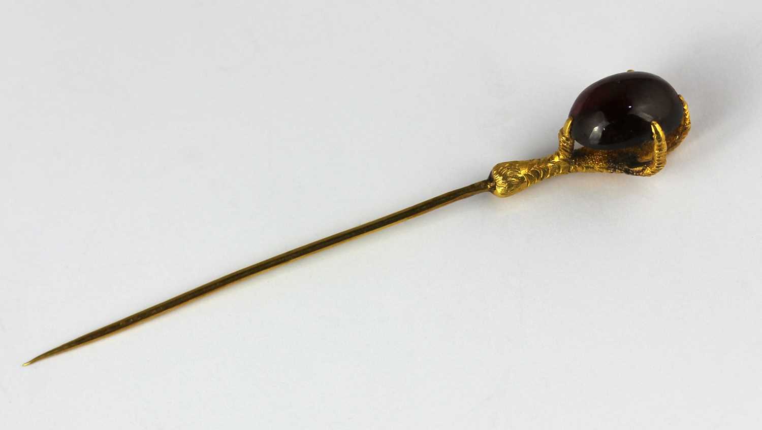 A gold and carbuncle garnet single stone stick pin designed as a claw holding an oval carbuncle