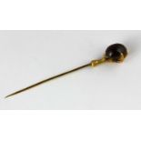 A gold and carbuncle garnet single stone stick pin designed as a claw holding an oval carbuncle