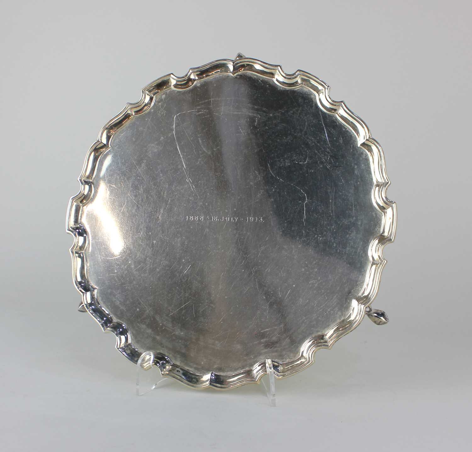 A George V silver salver with pie crust border, engraved inscription, on three hoof feet, maker