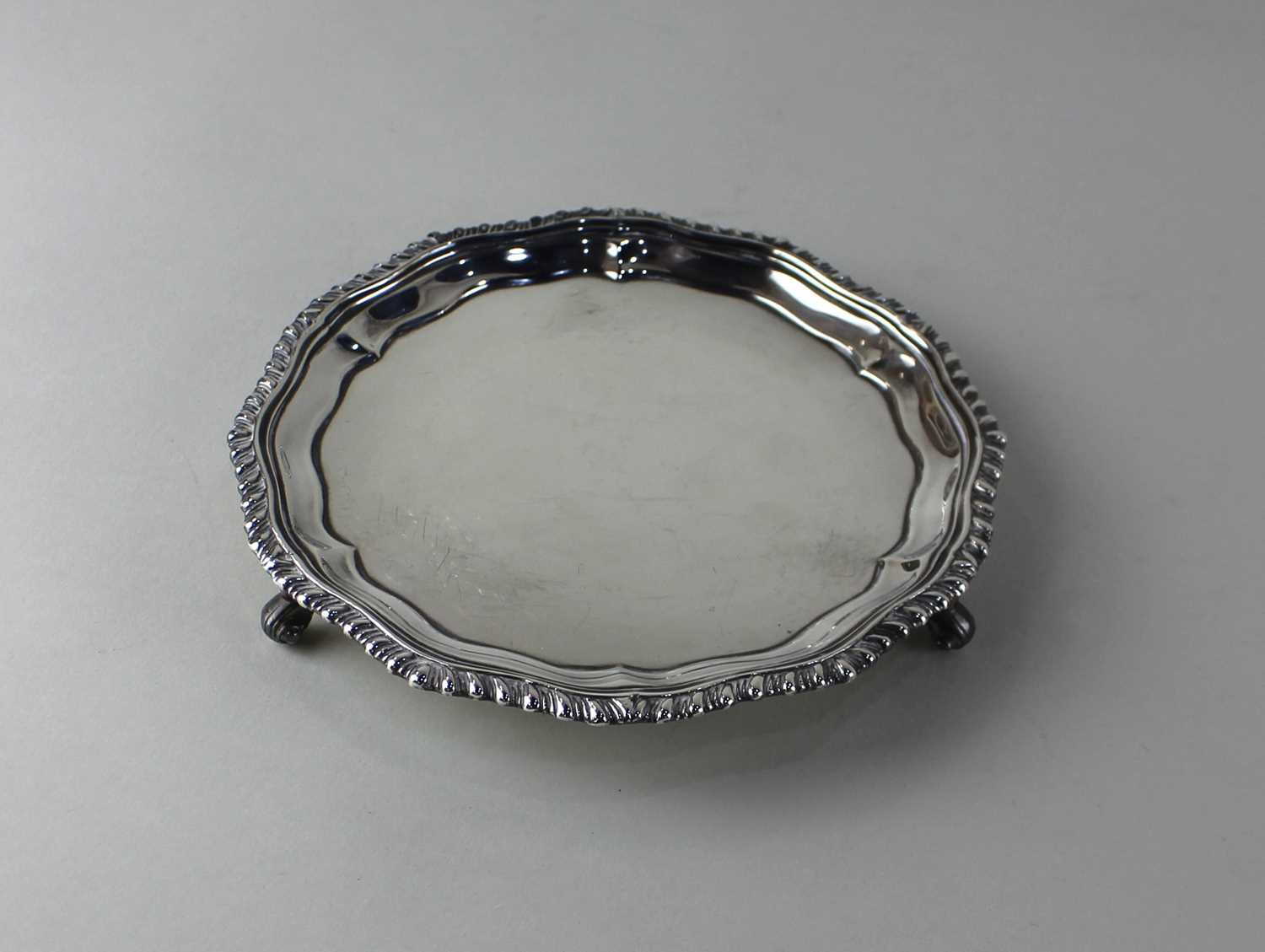 A George VI silver circular card tray with gadrooned pie crust border on three scroll feet, maker