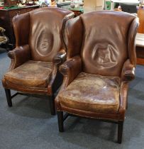 A pair of Georgian style brown leather wingback armchairs, with brass studs and solid wooden