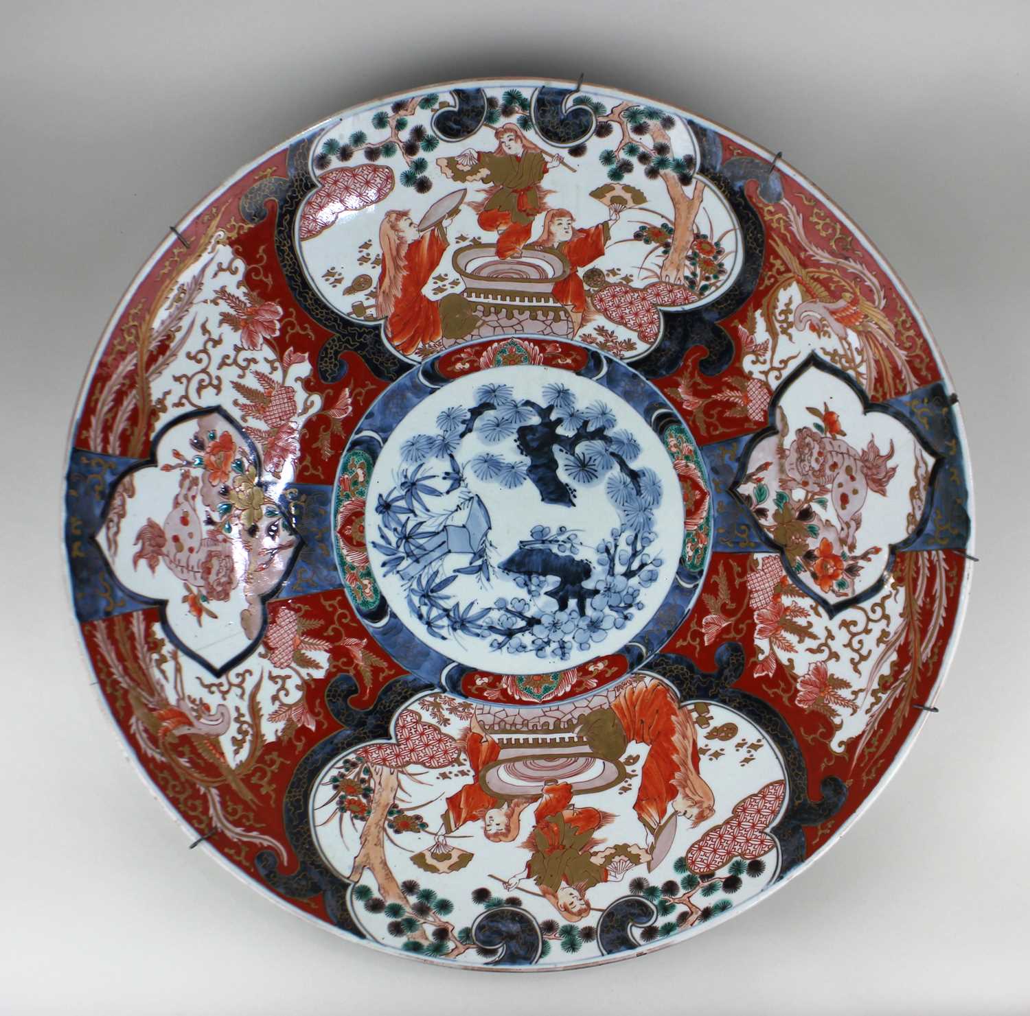 A large Japanese Imari ceramic charger decorated with panels of figures in a garden, character marks