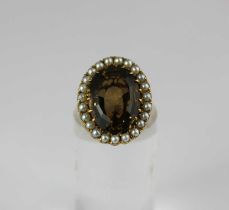 A 9ct gold ring claw set with an oval cut smoky quartz within a surround of half pearls, ring size