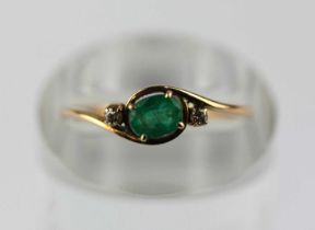 A gold, diamond and emerald ring set with a central emerald and two small diamonds in crossover