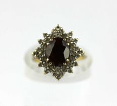 A 9ct gold, garnet and colourless gem shaped oval cluster ring, claw set with the oval cut garnet at