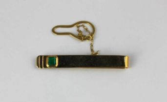 A gold and emerald single stone tie slide mounted with a rectangular cut emerald with a button