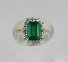 An 18ct gold emerald and diamond cluster ring, claw set with the rectangular step cut emerald in a