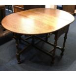 An oak gateleg table, oval shaped top with two drop flaps above a small drawer, on turned supports