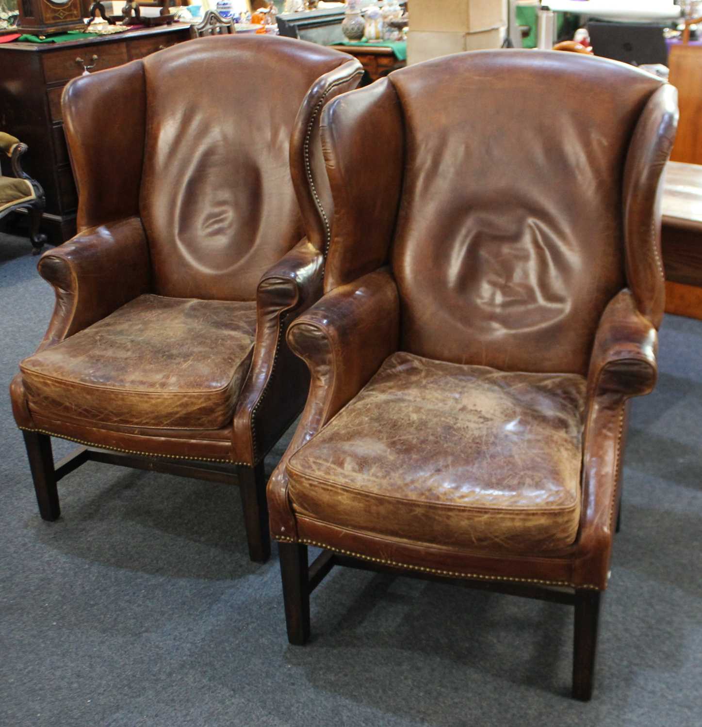 A pair of Georgian style brown leather wingback armchairs, with brass studs and solid wooden