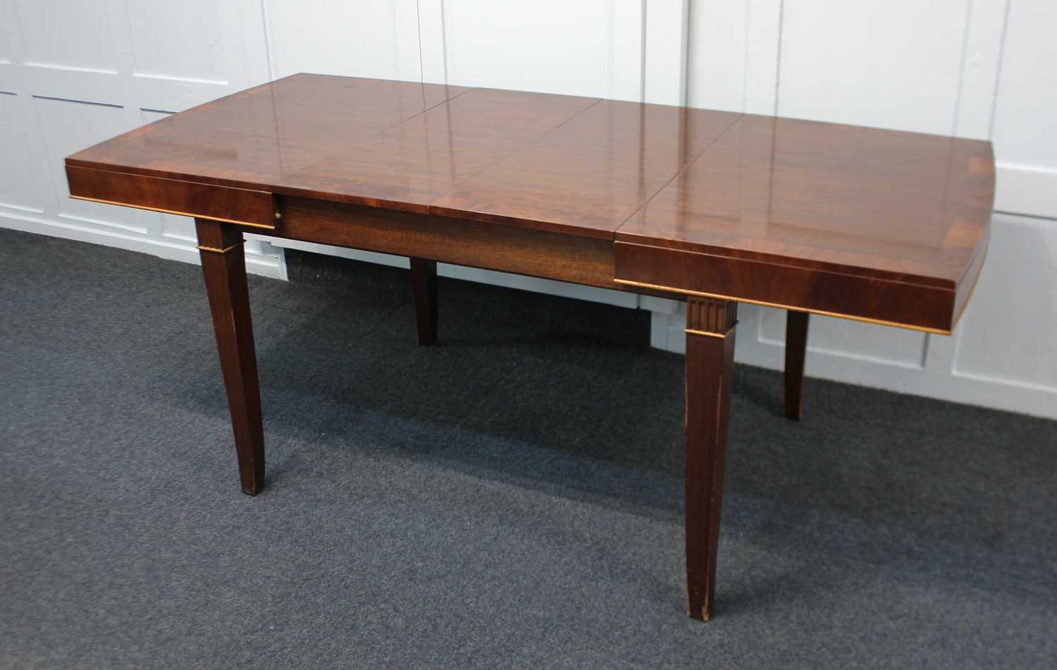 An Edwardian mahogany two leaf extending dining table, the crossbanded shaped rectangular top on