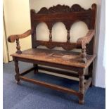 A carved oak bench with open arched back and scroll arms, on baluster supports and low stretcher,