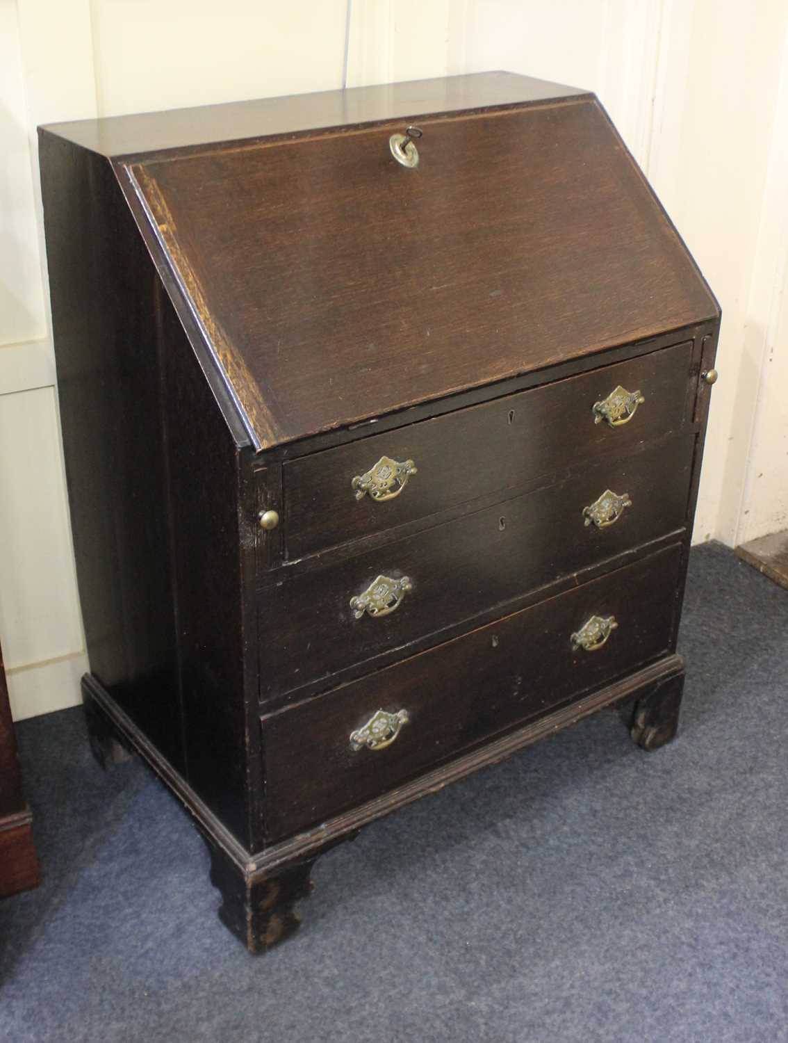 A George III oak bureau with three drawers with brass drop handles and pierced escutcheons, on