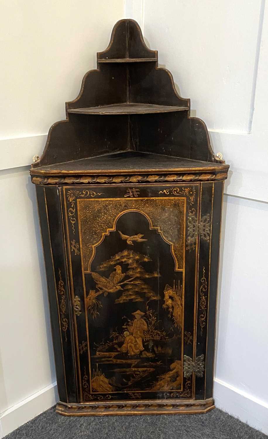 A Chinoiserie black lacquered corner cupboard the panel door decorated with gilt scene of figures