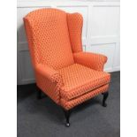 An upholstered wing back armchair on cabriole feet