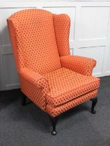 An upholstered wing back armchair on cabriole feet