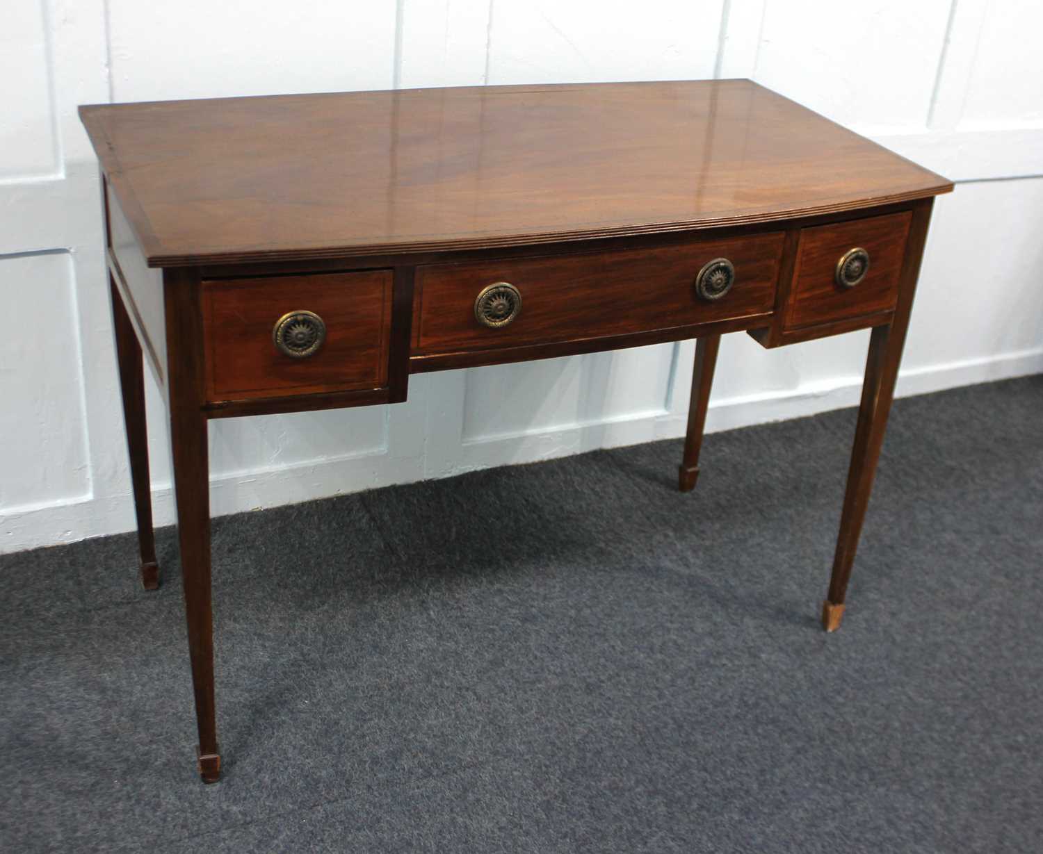 An Edwardian mahogany bowfront desk with an arrangement of three drawers on square tapered legs to