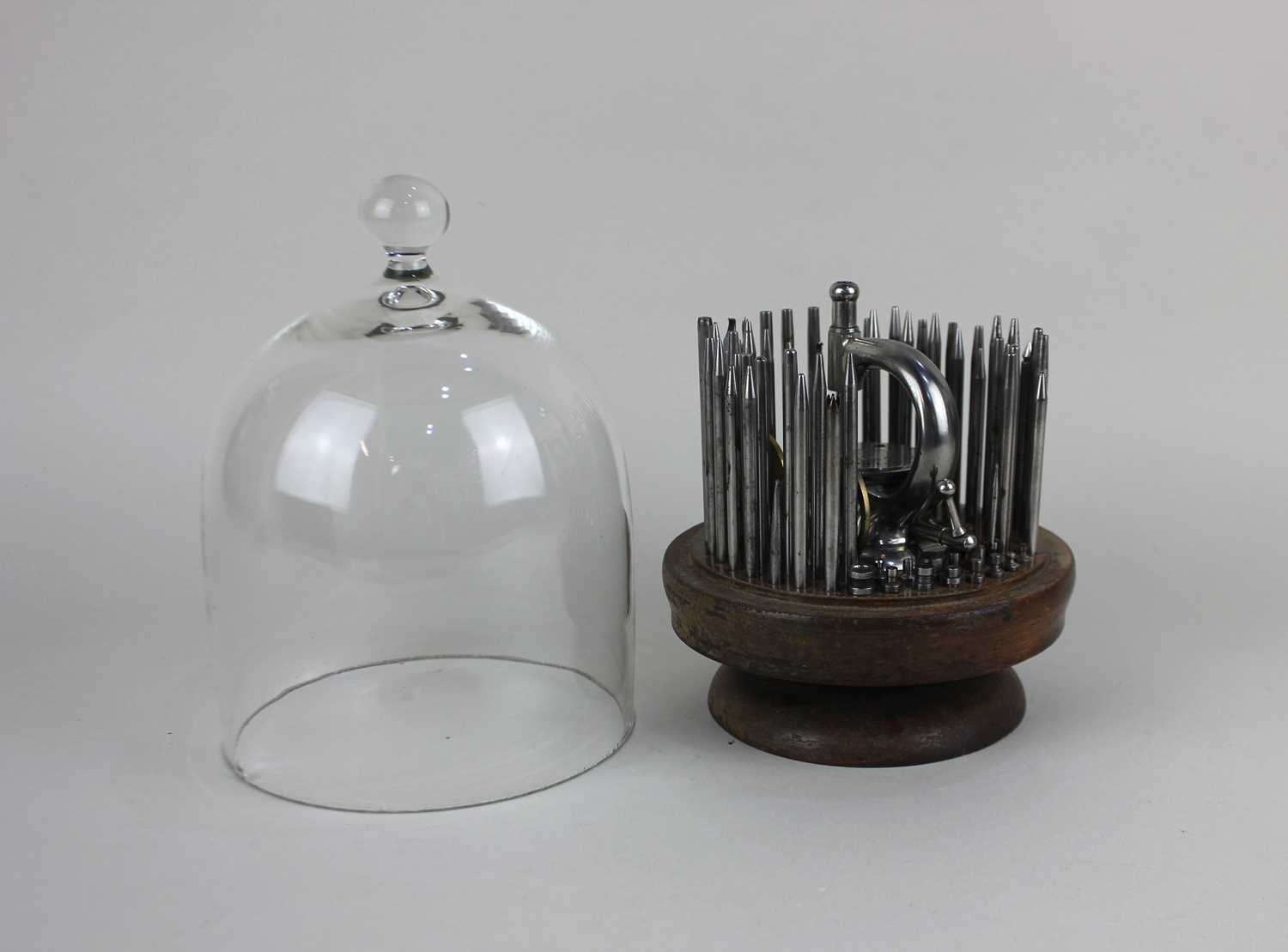 A watchmaker's rivett staking tool set on wooden stand under a glass cloche (cloche replaced)