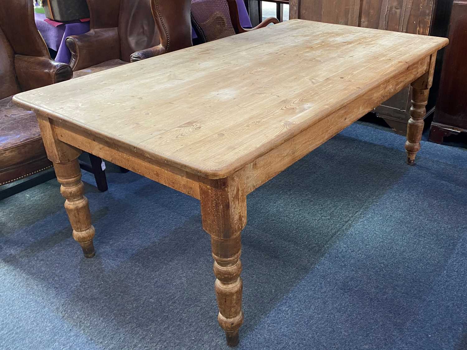 A pine farmhouse kitchen table, the rectangular plank top with rounded corners on turned legs