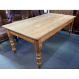 A pine farmhouse kitchen table, the rectangular plank top with rounded corners on turned legs