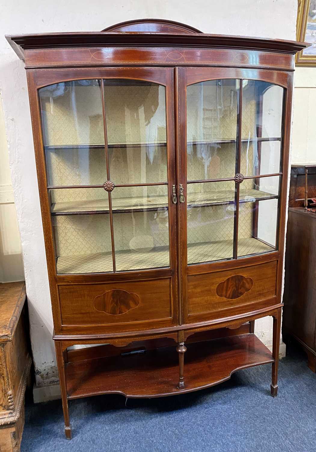 An Edwardian mahogany bowfront display cabinet with two glazed panel doors enclosing two shelves,