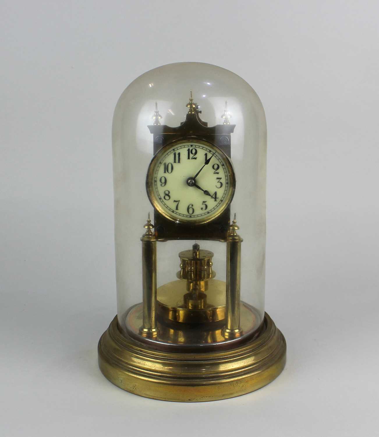 A gilt metal anniversary mantle clock under a glass dome on circular base, 29cm